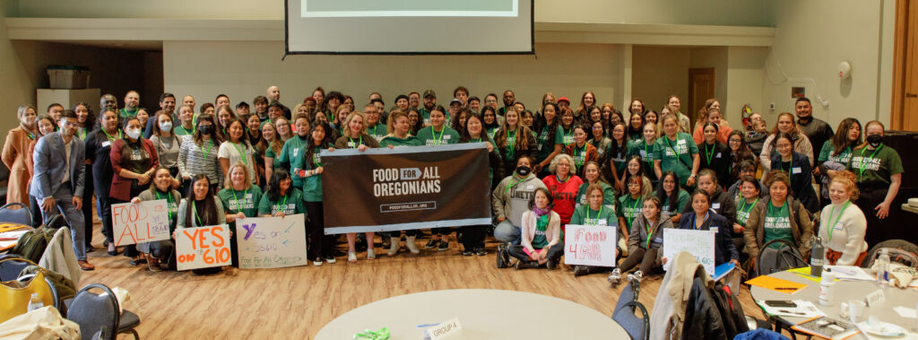 Dozens of supporters of the Food for All Oregonians bill gather in front of a sign for a photo